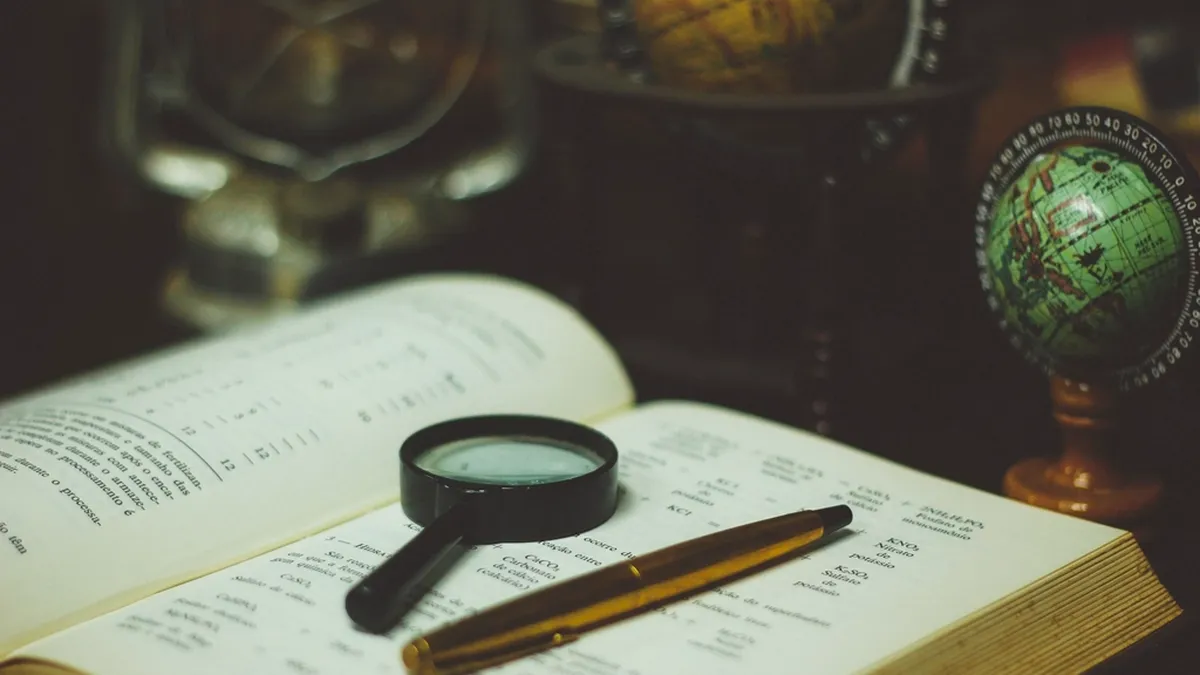 Lente d'ingrandimento d'epoca poggiata su un vecchio libro aperto, posta su un tavolo di legno scuro
