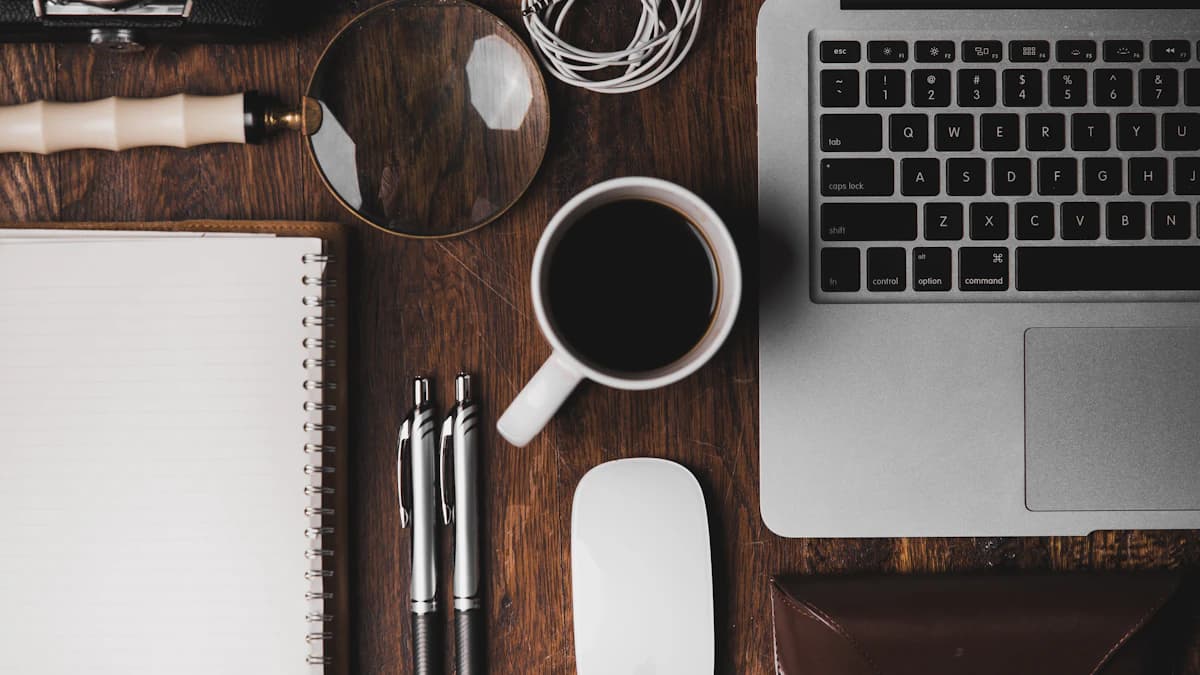 Un taccuino aperto con una penna accanto a una tazza di caffè su una scrivania in legno